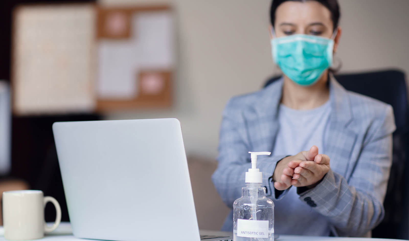 woman with mask on in front of laptop, sanitising her hands