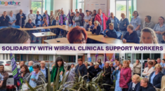 Solidarity with Wirral clinical support workers. Pay Fair for Patient Care. UNISON members hold flags at a meeting.