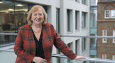Christina McAnea leans against a railing in UNISON centre, wearing a red patterned jacket