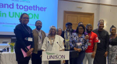 A group of Black members stand together in front of a conference banner with the words 'Stand together in UNISON'