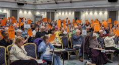 A group of retired members sitting in the conference hall, some holding voting cards in the air