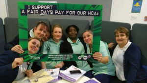 Healthcare workers hold up photo frame that reads 'I support a fair day's pay for our HCAs'