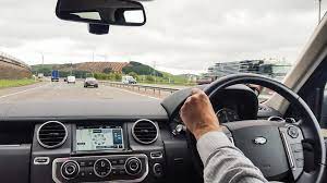 Photograph of a man at the wheel of a car – just a hand at the wheel and a view of a motorway