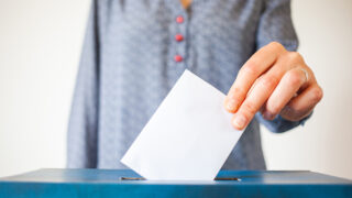 Hand of a woman putting a folded piece of paper in a ballot box