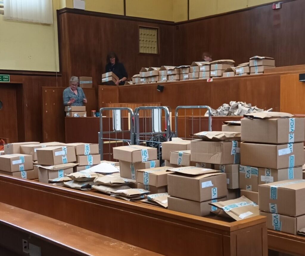 The team at Dorset Council election services taking whatever space is on offer - cardboard boxes piled high in what looks like a courtroom setup