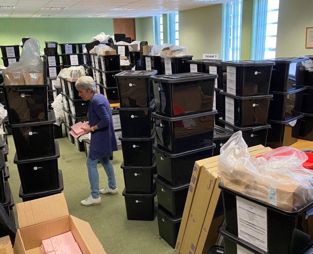The team at Dorset Council election services taking whatever space is on offer - Jacqui among towers of plastic boxes piled high in a large green walled room