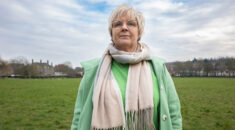 Portrait of Sam Thornton, standing in a park, with coat and scarf