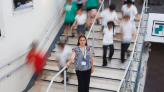 Clara Mason standing on some stairs, surrounding by children running down the stairs. The children are out of focus