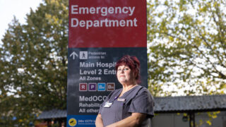 Portrait of Diane Coombs in front of a hospital entrance sign.