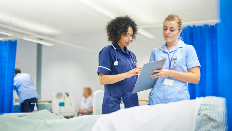 Two female nurses speaking with each other over a patient, who is out of shot