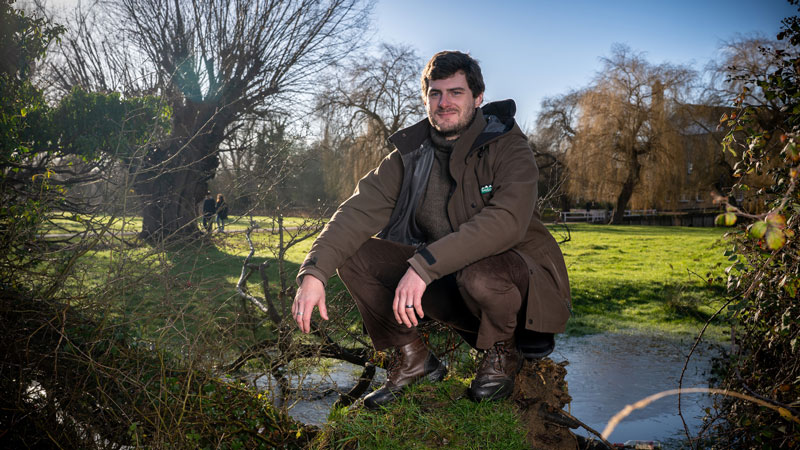 Photo of Ashley Dolling crouching down in a park, by the water and surrounded by trees