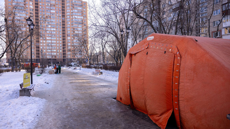 A large, unusual shaped orange tent on a snowy city street, with a tower block in the background