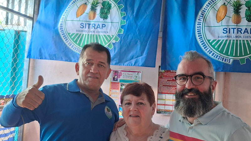 SITRAP general secretary Didier Leiton Valverde with Margaret McKee and James Anthony, standing in front of SITRAP banners on the wall 