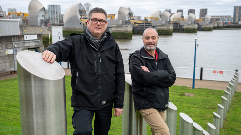 Steve Anderson and Mike Azzopardi, standing alongside each other and smiling, with the Thames Barrier behind them